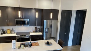 Una cocina moderna con armarios oscuros, electrodomésticos de acero inoxidable, iluminación colgante y una isla central con sillas.
