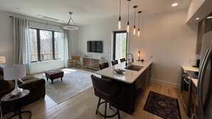 Una cocina moderna con una isla central, iluminación colgante y un comedor con sofá y sillas.
