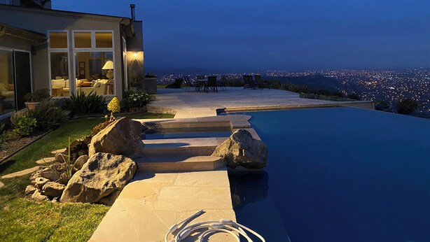 Una casa moderna con piscina, mobiliario exterior y vistas a la ciudad al anochecer.
