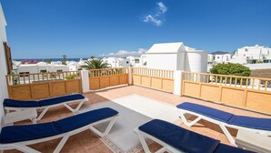 Una terraza en la azotea con sillones de sol, vista al mar y edificios blancos al fondo.