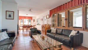 Una sala de estar con una mesa de centro de vidrio, sofás de cuero, un armario de madera y un comedor con una mesa y sillas.
