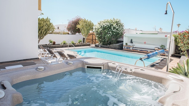 Un jacuzzi junto a una piscina, rodeado de sillas de descanso y plantas en macetas.