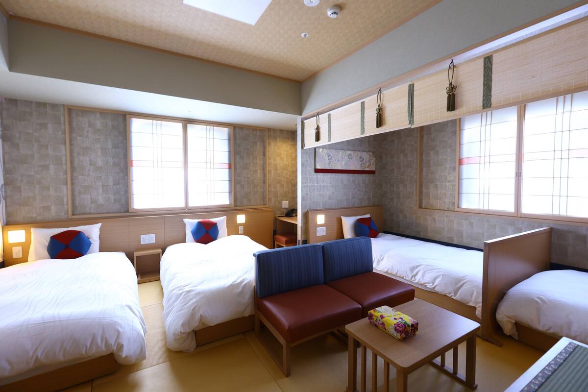 Habitación de hotel con dos camas individuales, un sofá, una mesita y ventana con vistas.