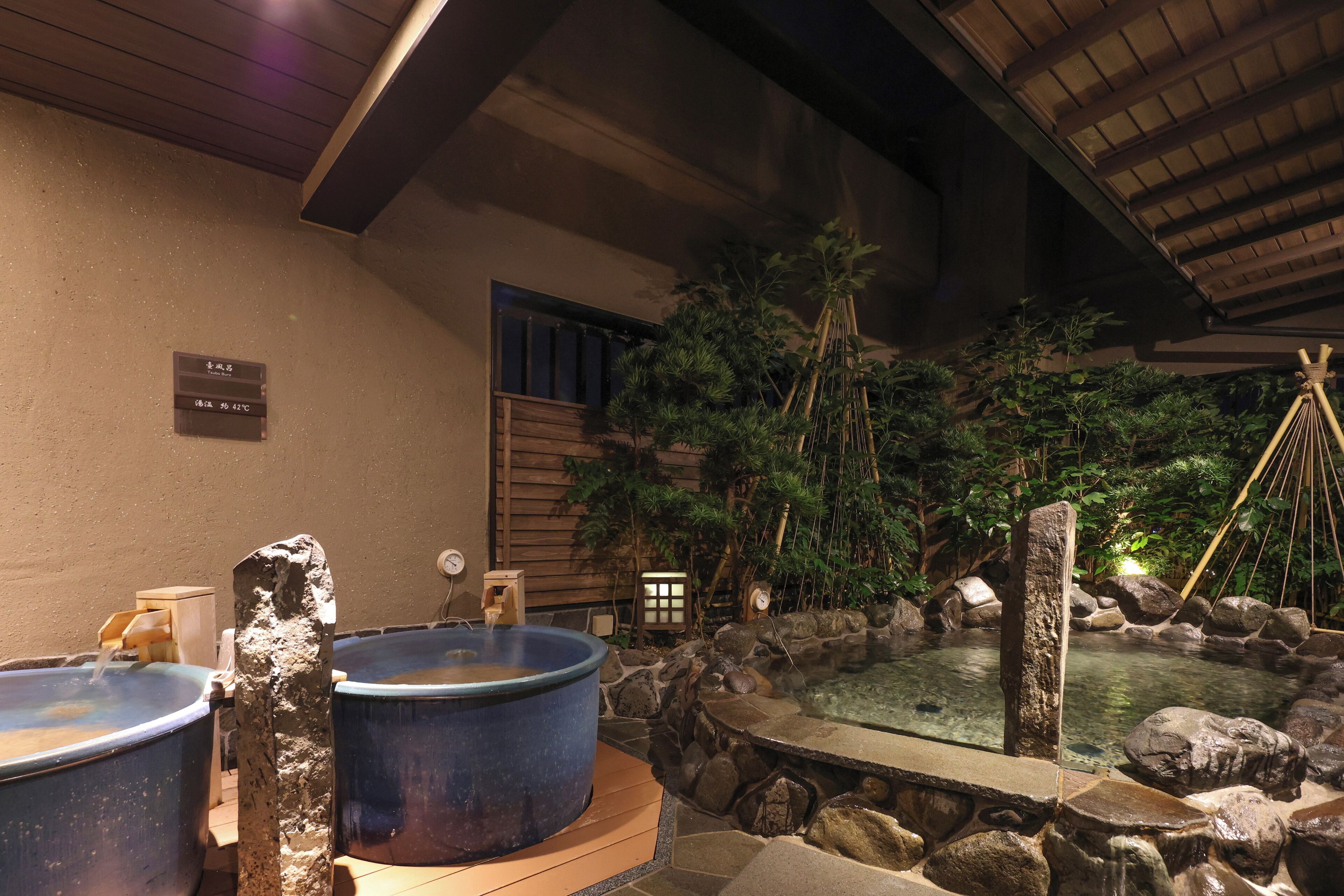 Ein traditionelles japanisches Onsen mit zwei großen Steingrößen, einer kleinen Holzstruktur und einem Steingarten.