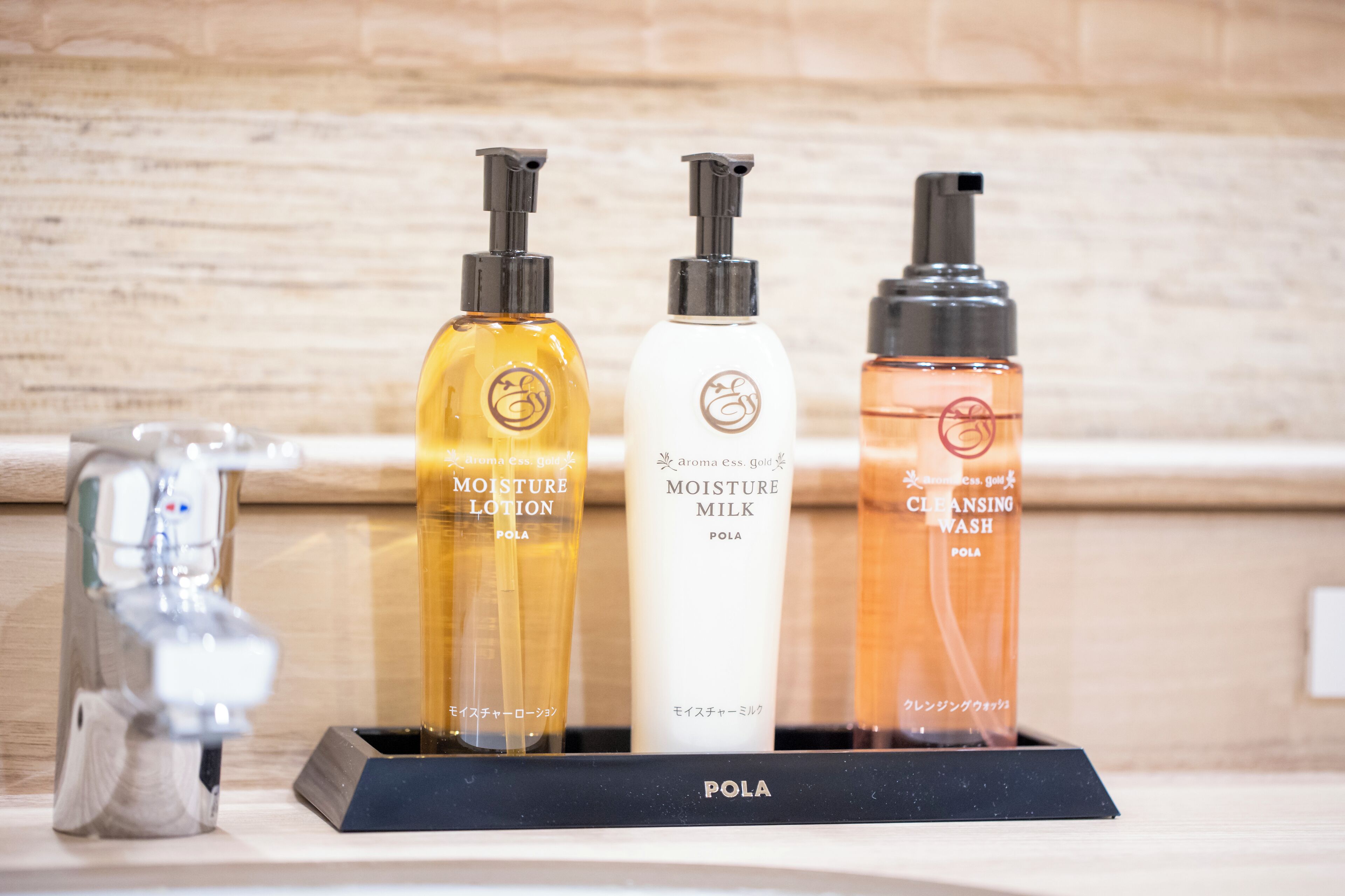 Three bottles of skincare products on a black tray labeled 'POLA' with a wooden background.