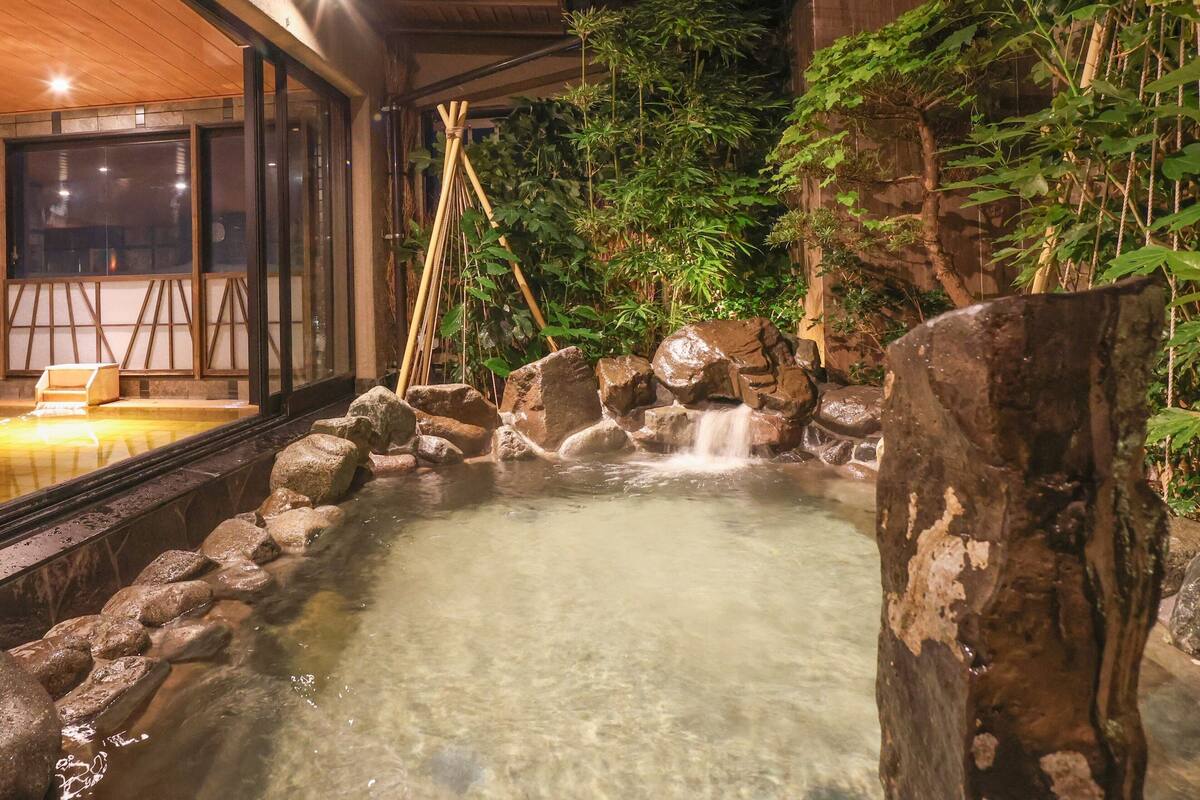 Un área de aguas termales con una terraza de madera, rocas y bambú.