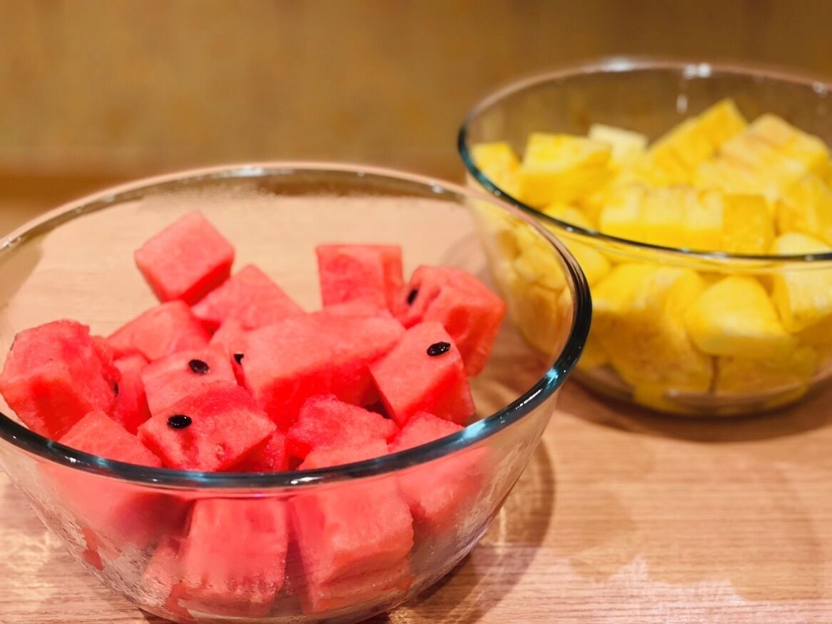 Deux bols en verre contenant des morceaux de pastèque et d’ananas, posés sur une surface en bois.