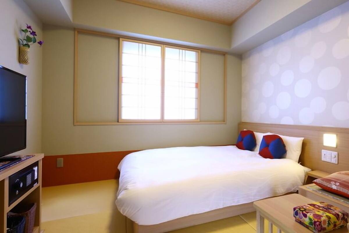 Una habitación de hotel con cama, televisión, ventana y pared con un diseño circular.