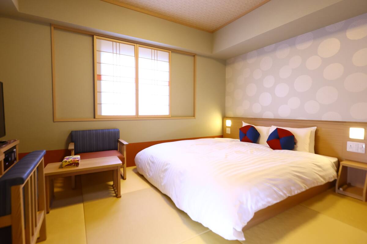 Habitación de hotel con cama, escritorio, silla, ventana y pared con estampado de lunares.