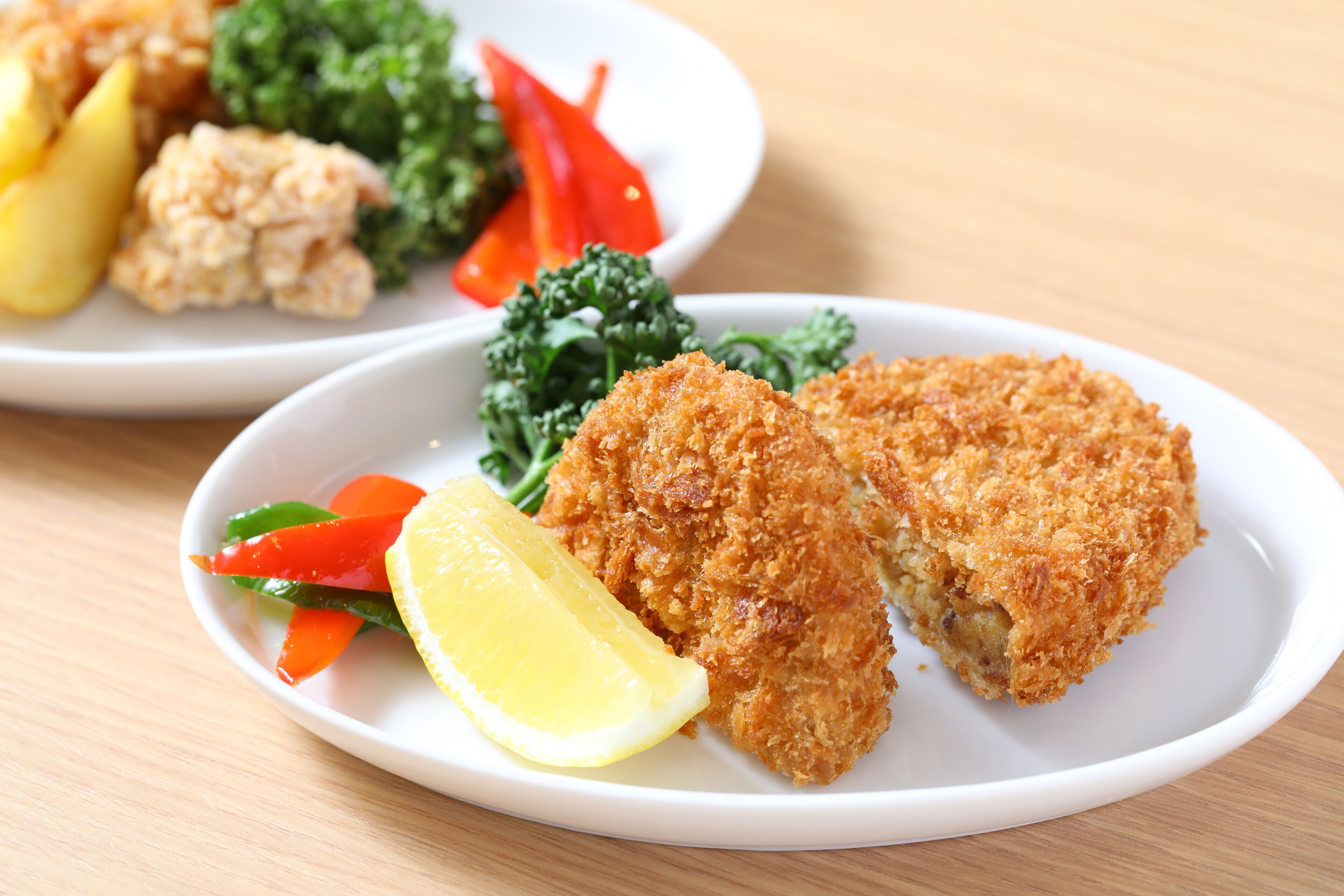A plate with breaded chicken cutlets, lemon wedge, and mixed vegetables.