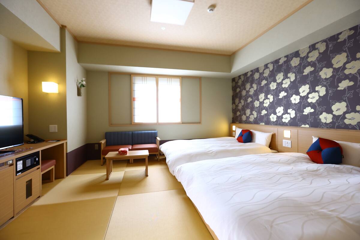 Una habitación de hotel con cama, escritorio, televisor y ventana.