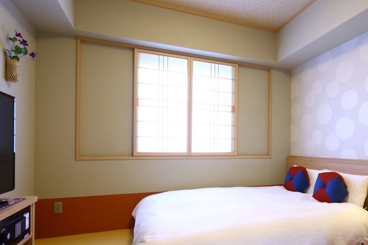 Habitación de hotel con una cama, televisión, ventana y pared con estampado de lunares.