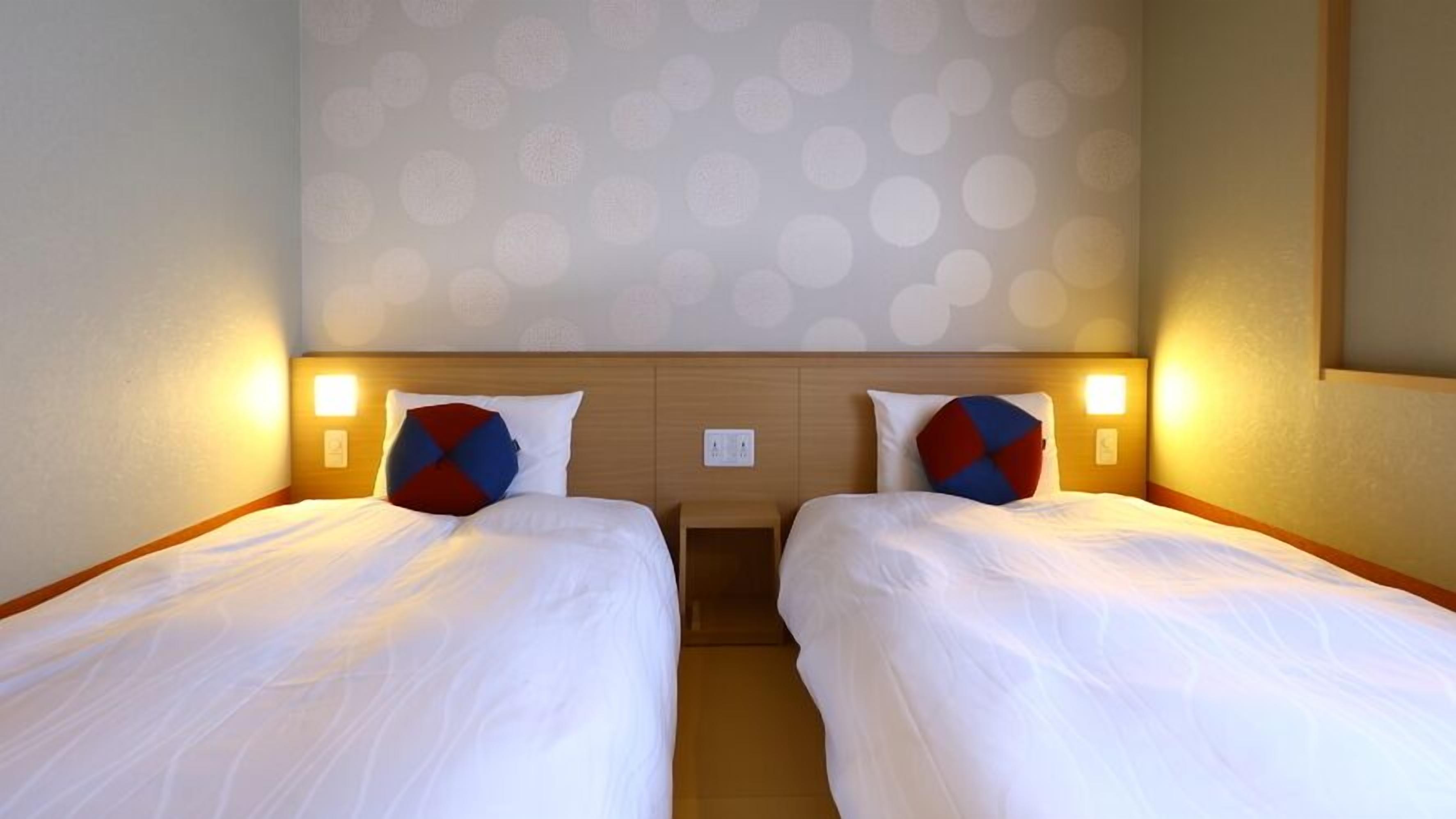 A hotel room with two single beds, each with a pillow and a bedside table.