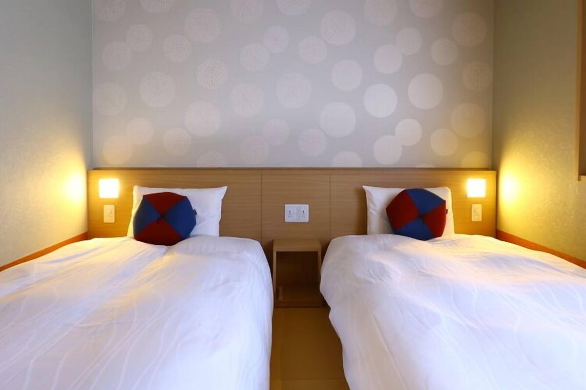 Habitación de hotel con dos camas individuales, cada una con una almohada y una mesita de noche.
