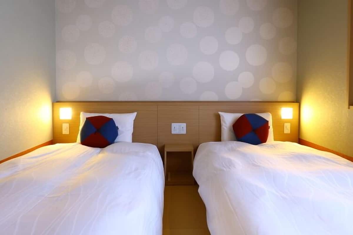 A hotel room with two single beds, each with a pillow and a bedside table.
