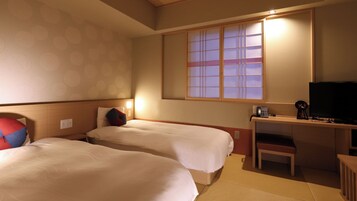 Una habitación de hotel con dos camas, un escritorio con televisor, teléfono y una mesita.