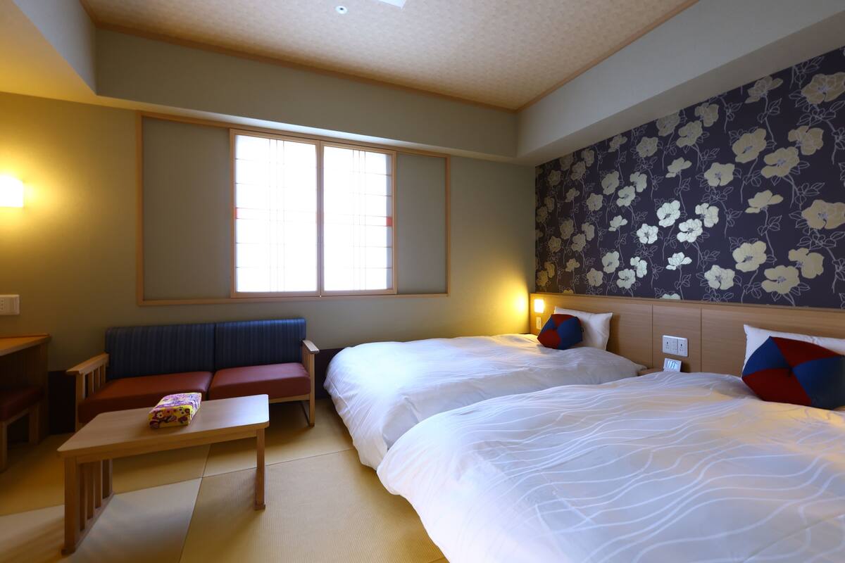 Una habitación de hotel con dos camas, un sofá, una mesita y un ventanal grande.