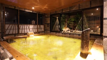 A traditional Japanese onsen with a wooden deck, stone walls, and a view of the surrounding nature.
