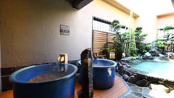 Un área de aguas termales con tinas azules grandes y una piscina pequeña, rodeada de elementos de piedra y madera.