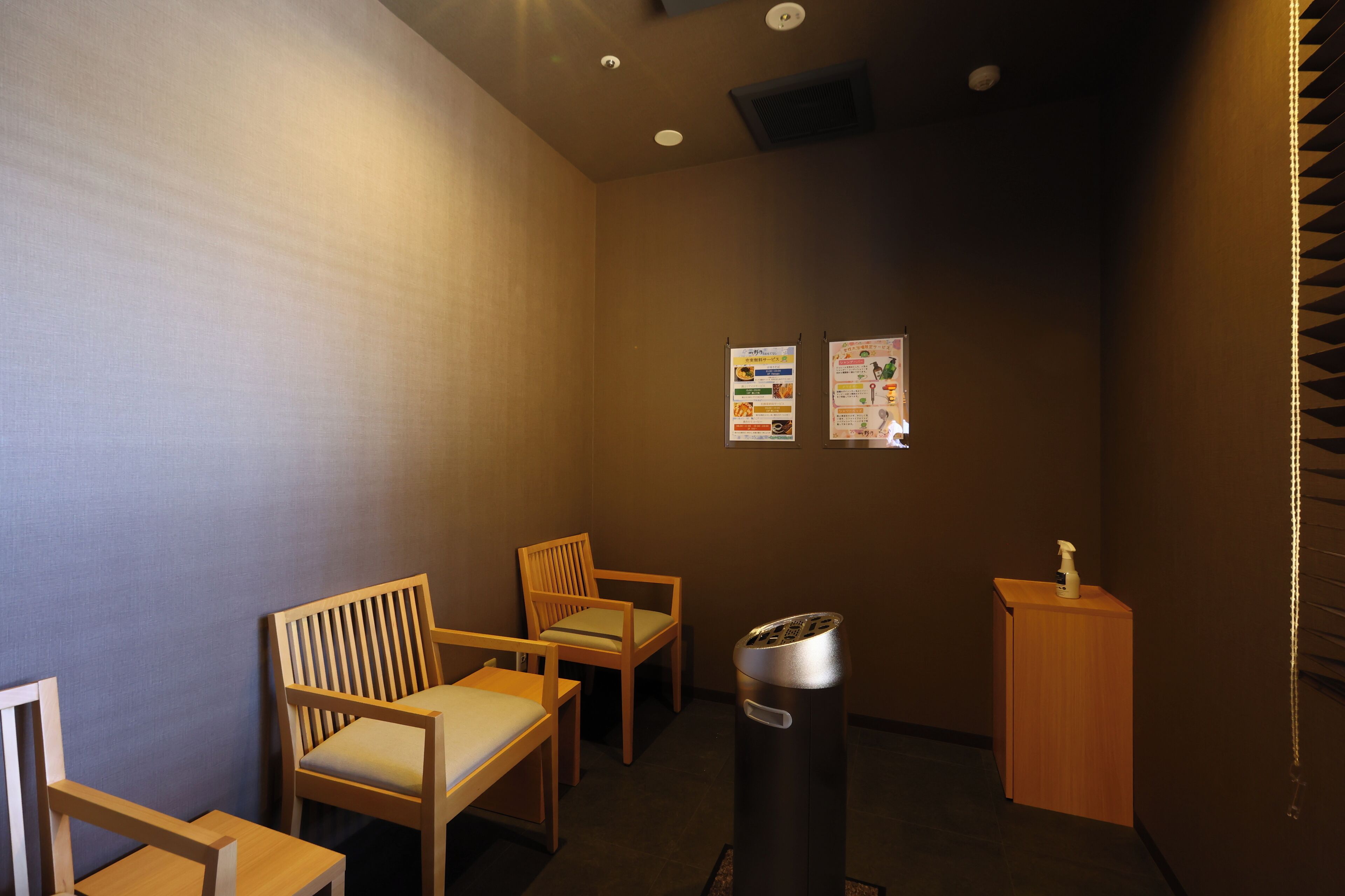 A room with two wooden chairs, a trash bin, and a small wooden table with a bottle on it.