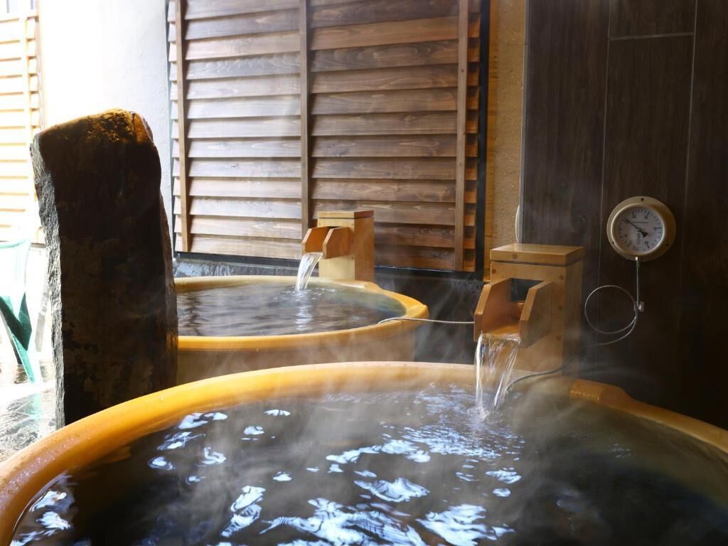 Un onsen japonés tradicional con varias piscinas termales, bancos de madera y un reloj en la pared.