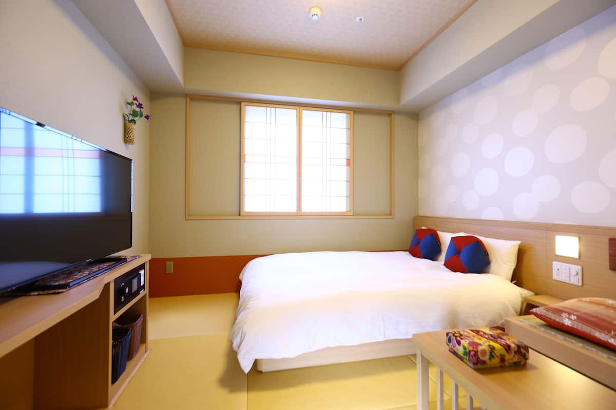 Una habitación de hotel con cama, televisión y ventana con persianas.