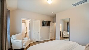 Una camera d'albergo con un letto grande, un'area salotto con una poltrona, una televisione a parete e uno specchio.