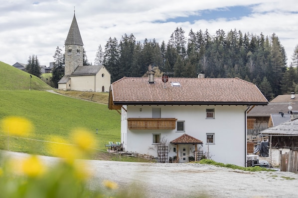 Un bâtiment blanc avec un toit recouvert de tuiles rouges, un petit balcon et une clôture en bois à l’avant.