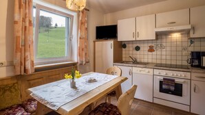 Een keuken met een eettafel, stoelen, een televisie en uitzicht op een groen veld.