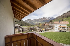 Un balcon doté d’une balustrade en bois, d’où l’on peut admirer un village rural avec des maisons et des montagnes en arrière-plan.
