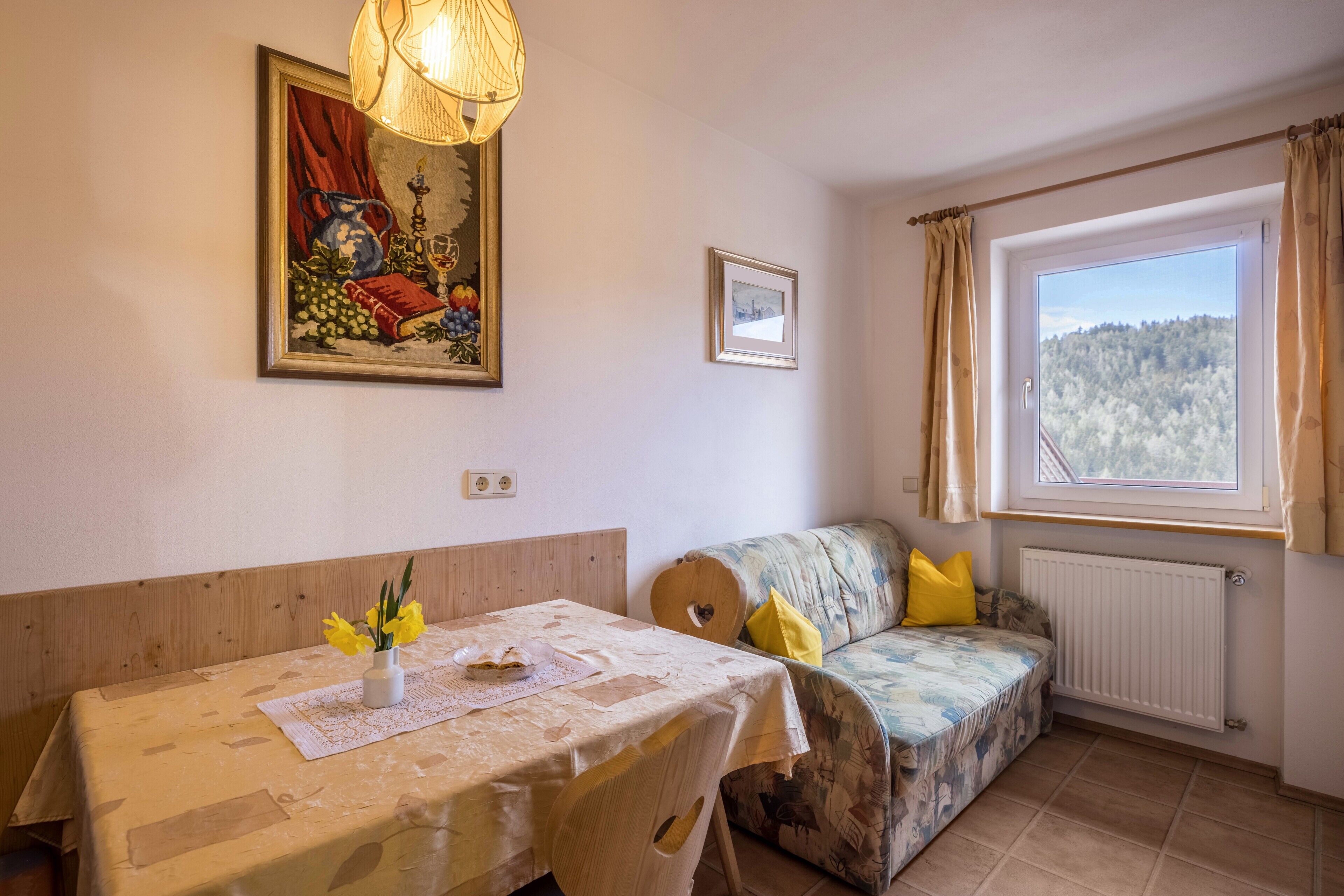 A room with a dining table, a sofa, a window with a view, and a painting on the wall.