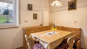 Een eethoek met een tafel, stoelen, een bank, een hanglamp en ingelijste foto's aan de wanden.