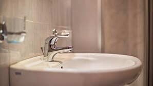 Een badkamer met een witte wastafel, een chromen kraan en een douchecabine van glas.