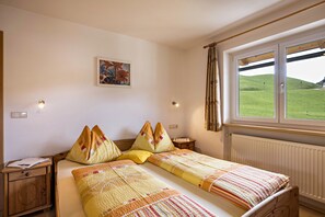Un letto matrimoniale con lenzuola a fantasia, un comodino con una lampada, un quadro appeso al muro e una finestra che si affaccia su dolci colline verdi.