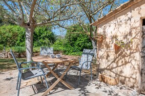 Une terrasse extérieure avec une table et des chaises en bois, entourée d’un sol en pierre et de verdure.