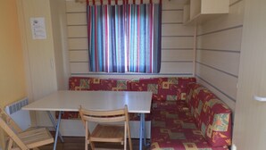 A compact kitchenette with a white countertop, a wooden chair, and a bench with a patterned cushion. - Landshause Bungalow T3 - A05 (Pataias)