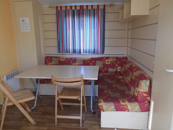Une petite cuisine équipée avec un plan de travail blanc, une chaise en bois et un banc agrémenté d’un coussin à motifs.