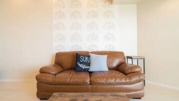 A brown leather sofa with two pillows, one with text, in a room with a patterned wallpaper and a small side table.