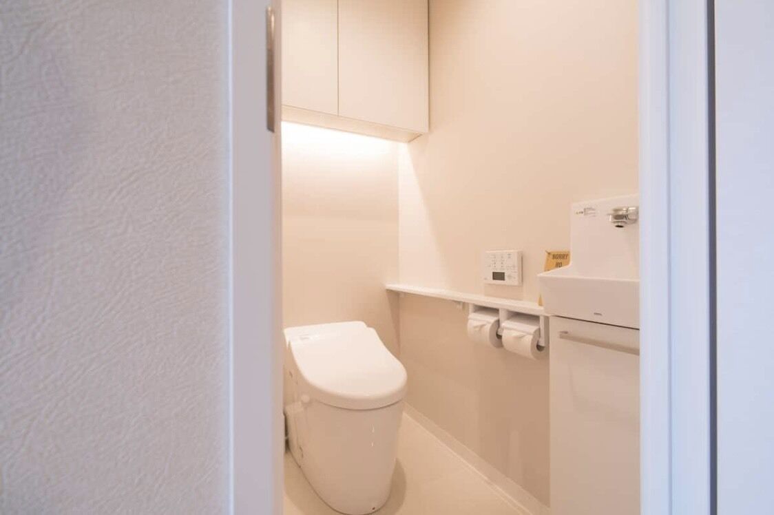 A small, clean bathroom with a toilet, a shelf with toiletries, and a wall-mounted cabinet.