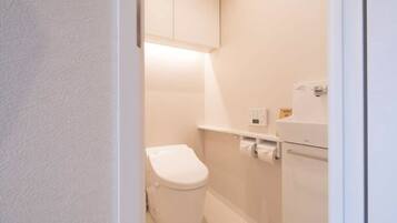 A small, clean bathroom with a toilet, a shelf with toiletries, and a wall-mounted cabinet.