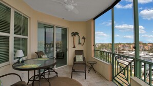 A balcony with a glass door leading to a dining area, a ceiling fan, and a view of boats and buildings. - Your Waterfront Retreat at Burnt Store Marina (Punta Gorda)