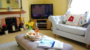 Ein Wohnzimmer mit einem weißen Sofa, einem Tablett mit Getränken und einem Buch, einem Fernseher und einem Kamin.