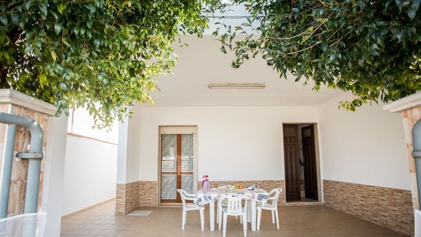 A covered patio area with a tiled floor, a table with chairs, and a door.