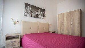 A bedroom with a bed, a nightstand, a wooden wardrobe, and a cityscape painting on the wall.