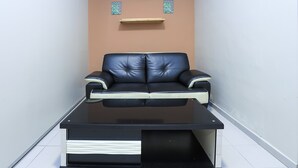 A modern living room with a black leather sofa, a glass coffee table, and a wooden shelf on the wall. - OYO HOME 90244 Dkeris 2bhk Apartment (Malacca City)
