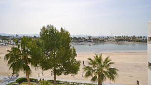 A beach view with palm trees, a sandy beach, and a calm sea. - Alcúdia Sea - Modern apartment on the seafront in Alcúdia, Mallorca (Alcúdia)