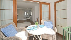 A balcony with wicker furniture, a small table with plates and a plant, and a view into the house. - Alcúdia Sea - Modern apartment on the seafront in Alcúdia, Mallorca (Alcúdia)