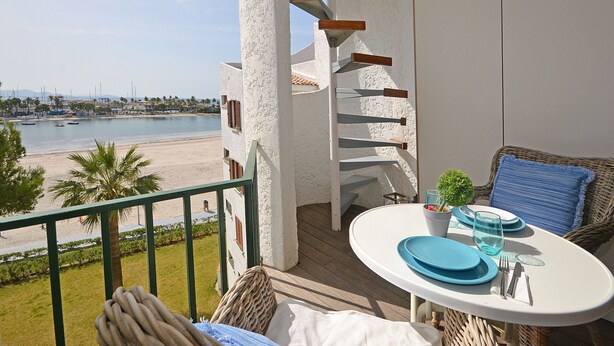 A balcony with a table set for two, overlooking a beach and a marina. - Alcúdia Sea - Modern apartment on the seafront in Alcúdia, Mallorca (Alcúdia)