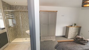Un dormitorio con ducha, una cama con edredón floral, un armario gris y una mesita de noche con un florero.