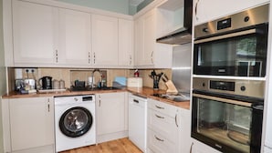 A compact kitchen with white cabinets, a washing machine, a dishwasher, and a double oven. - Ty Capel (Betws-Y-Coed)
